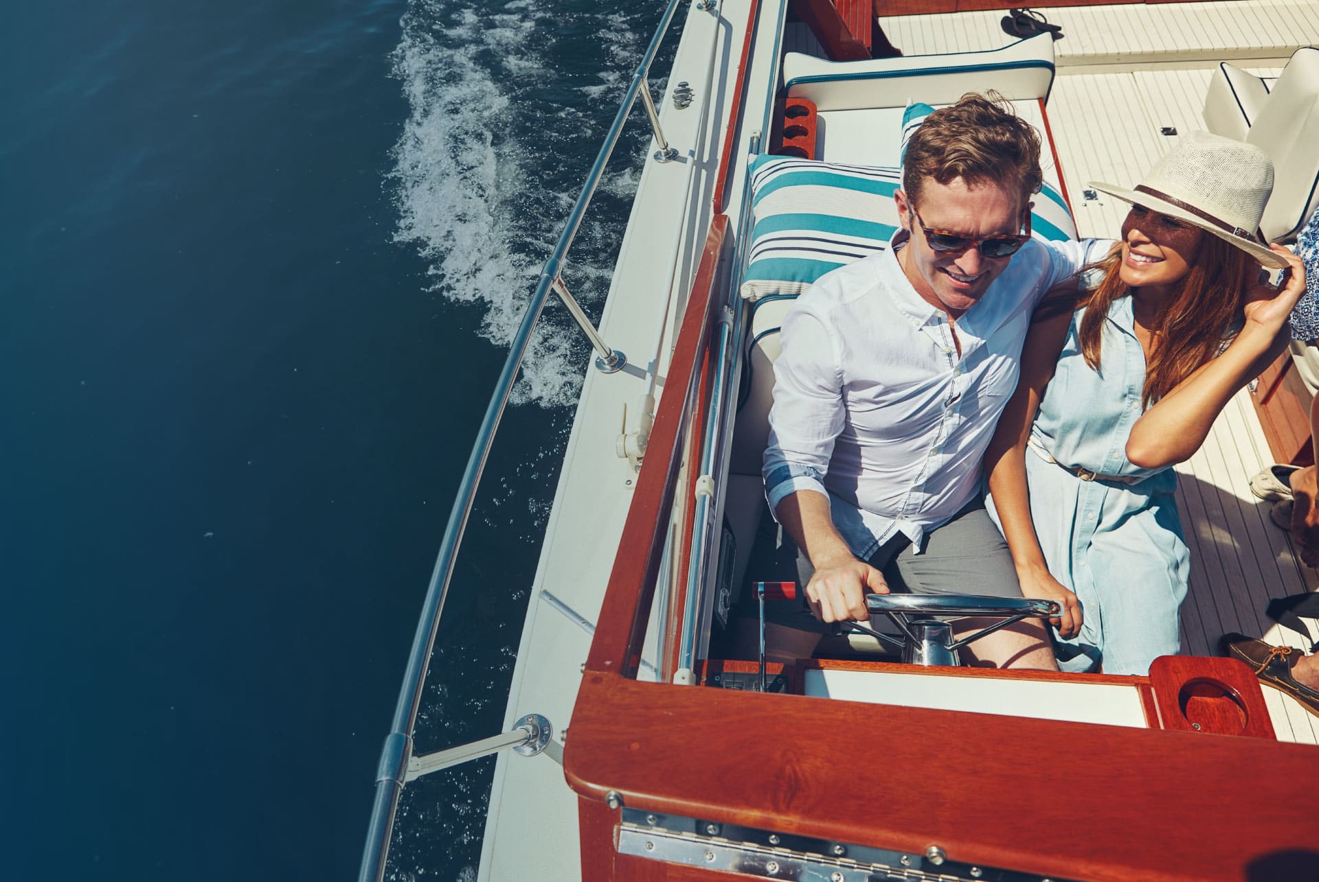 Man and woman driving a boat with mahogany trim and chrome railing.