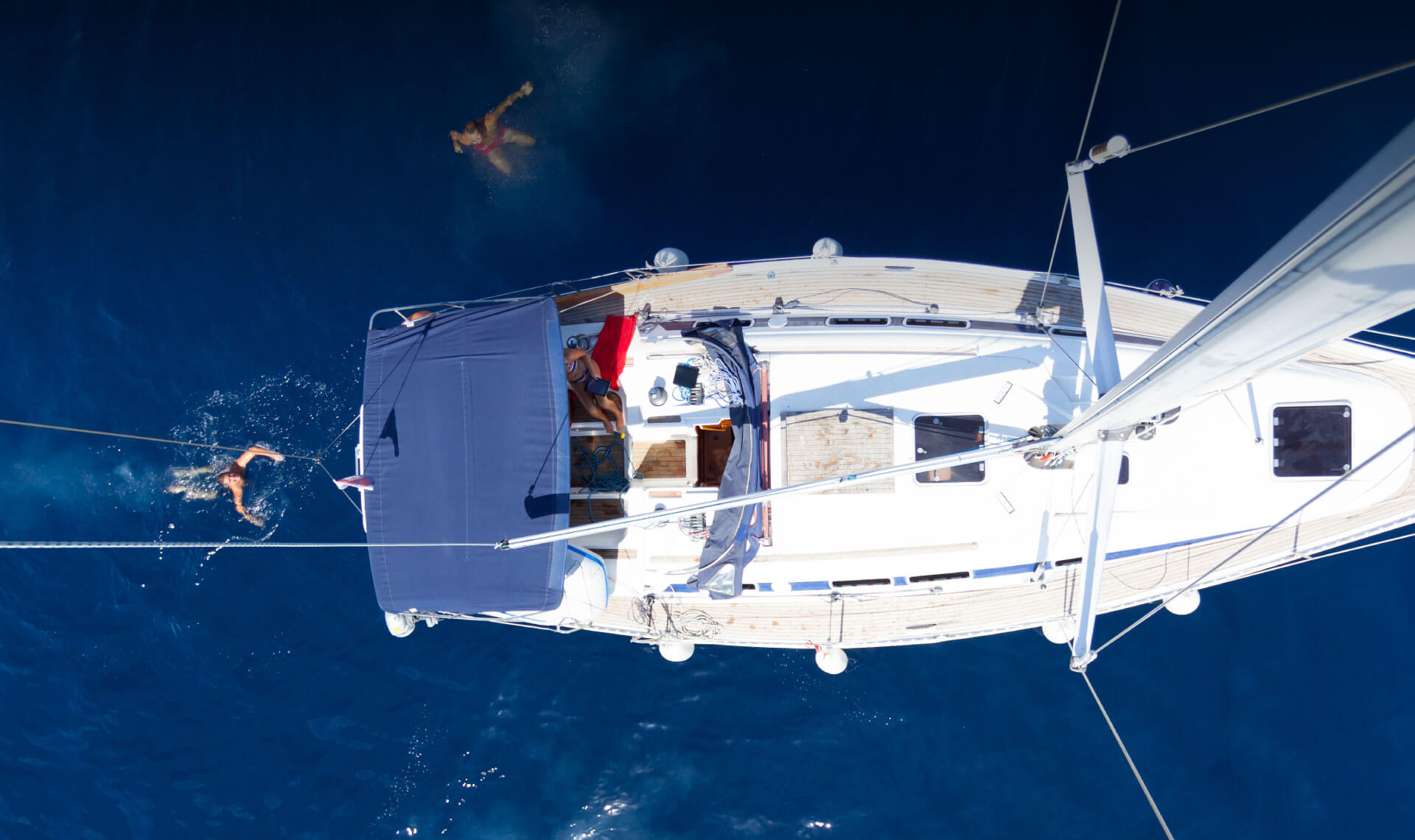 Bird's eye view of people swimming around a sailboat.