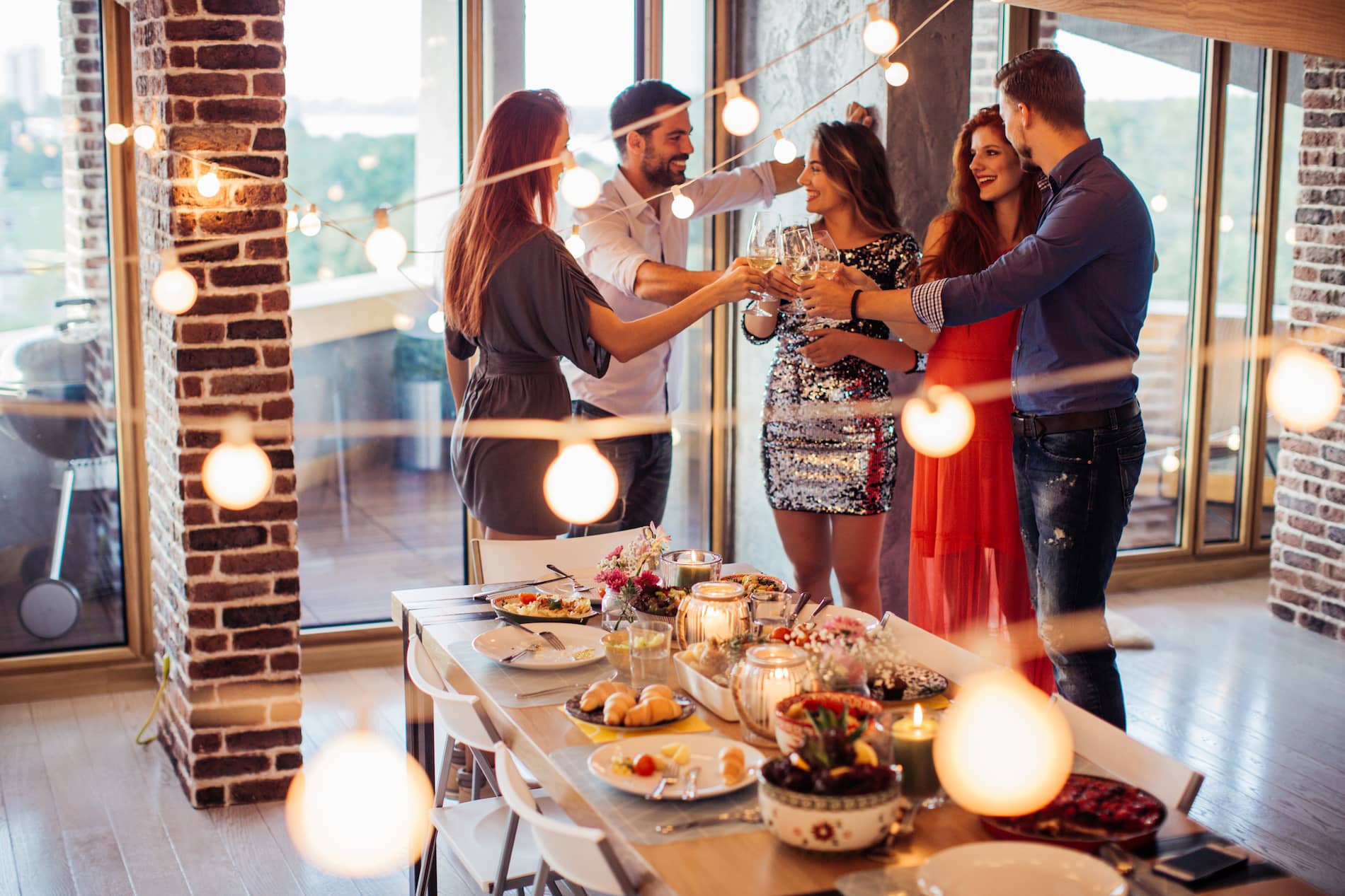 Friends dressed in cocktail and business casual attire at a dinner party toasting with wine glasses.