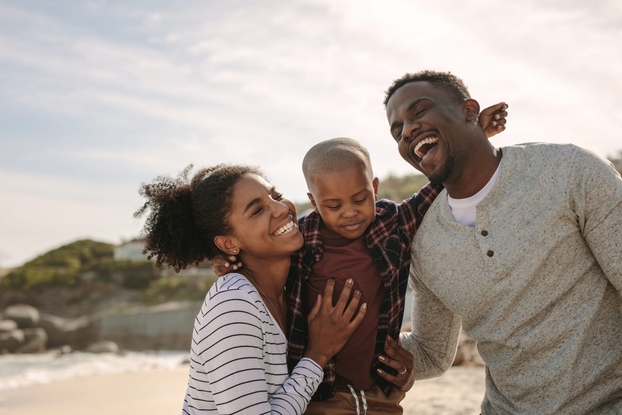 Man and woman holding a toddler while laughing on the beach.